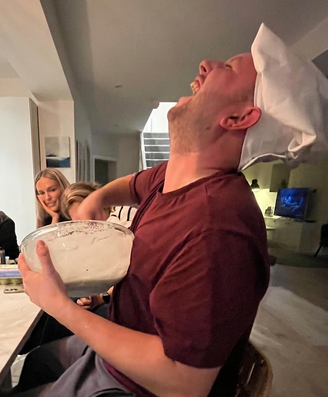 A guest laughing in a chef hat during an in home cookery lesson